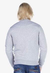 Grijze sweatshirt met een geribde ronde hals en manchetten, voorzien van een zak op de linkermouw. Zachte stof met een gladde textuur.