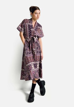 Purple patterned dress with short sleeves, a tie waist, and a flowing design. Worn with black platform shoes and knee-high socks.