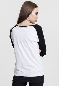 Svart og hvit raglan-skjorte med lange ermer, bomullstoff, rund hals, synlig søm og uformell passform.