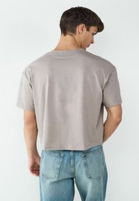 Szara krótka koszulka z gładkiego bawełnianego materiału, z krótkim rękawem i luźnym krojem, w połączeniu z jasnoniebieskimi, zniszczonymi dżinsami.