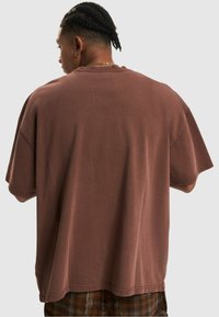 Oversized brown cotton t-shirt with short sleeves, a relaxed fit, and a simple crew neckline. No visible patterns or graphics.