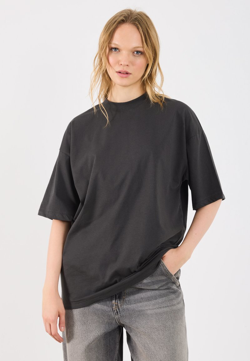 Camiseta oversized preta feita de algodão, com mangas curtas e decote redondo, combinada com jeans cinza claro com desbotamento.