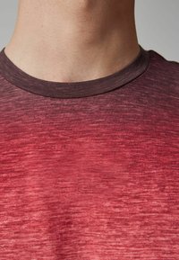 Camiseta de manga corta en un color rojo degradado con un acabado texturizado, que presenta un cuello redondo y una cinta de color burdeos oscuro.