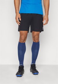 Fekete sportnadrág, kék rövid ujjú póló, kék, vádliig érő zoknik textúrával, és fekete cipők kék részletekkel.