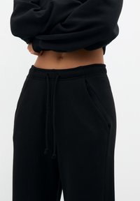 Un pantalon de survêtement noir en matériau doux, avec une taille élastique avec cordons de serrage, des poches latérales et une coupe décontractée.