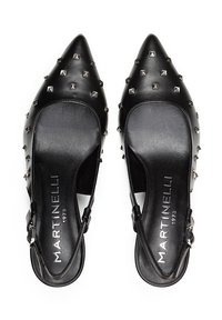 Zapatos de piel negra tipo slingback con punteras puntiagudas, múltiples tachuelas plateadas en la parte superior y una plantilla de marca. Textura suave y diseño minimalista.
