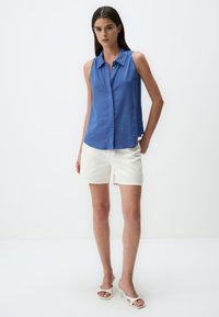 Blaues ärmelloses Hemd mit Knopfleiste, kombiniert mit weißen Shorts. Das Hemd hat einen Kragen und einen lockeren Schnitt und besteht aus leichtem Material.