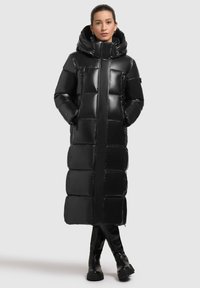 Geacă puf neagră cu un design lung, finisaj lucios, guler înalt și glugă. Prezintă buzunare cu fermoar și un model matlasat pătrățos.