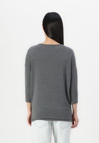 Grå T-shirt i bomullsblandning med lång ärm, avslappnad passform, rund halslinje och sänkta axlar, kombinerad med ljusblå jeans.