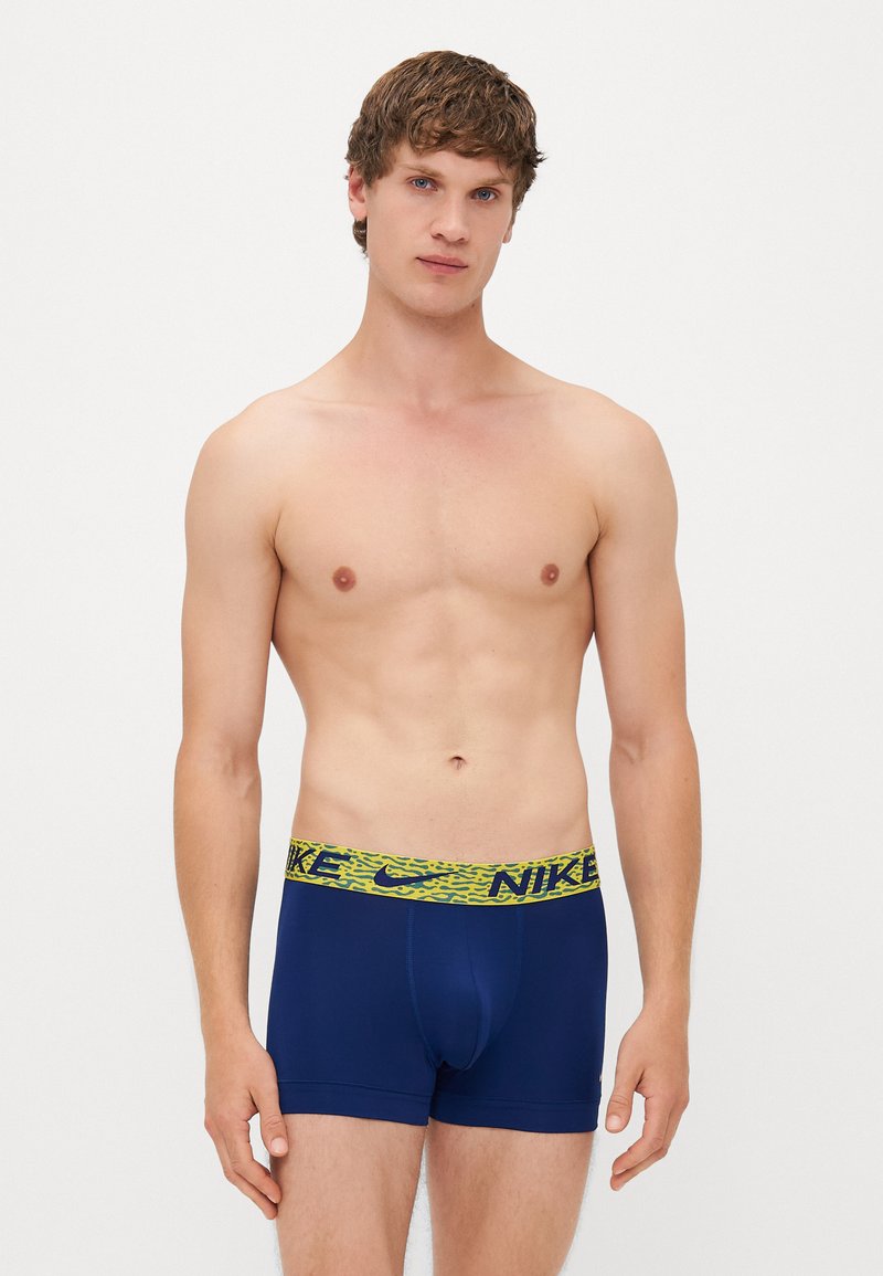 Mørkeblå boxer shorts med et gult-grønt mønster på kanten, der fremhæver Nike-logoet. Lavet af glat, strækbart stof for komfort.