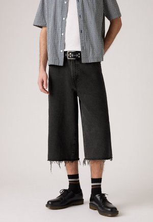 Svarte denim culotter med frynsete nederkant, parret med en rutete skjorte med korte ermer, svarte sko og stripete sokker.