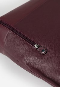 Borsa in pelle bordeaux con finitura strutturata, caratterizzata da una cerniera nera e un tirante in argento. Vista ravvicinata del dettaglio della chiusura con cerniera.