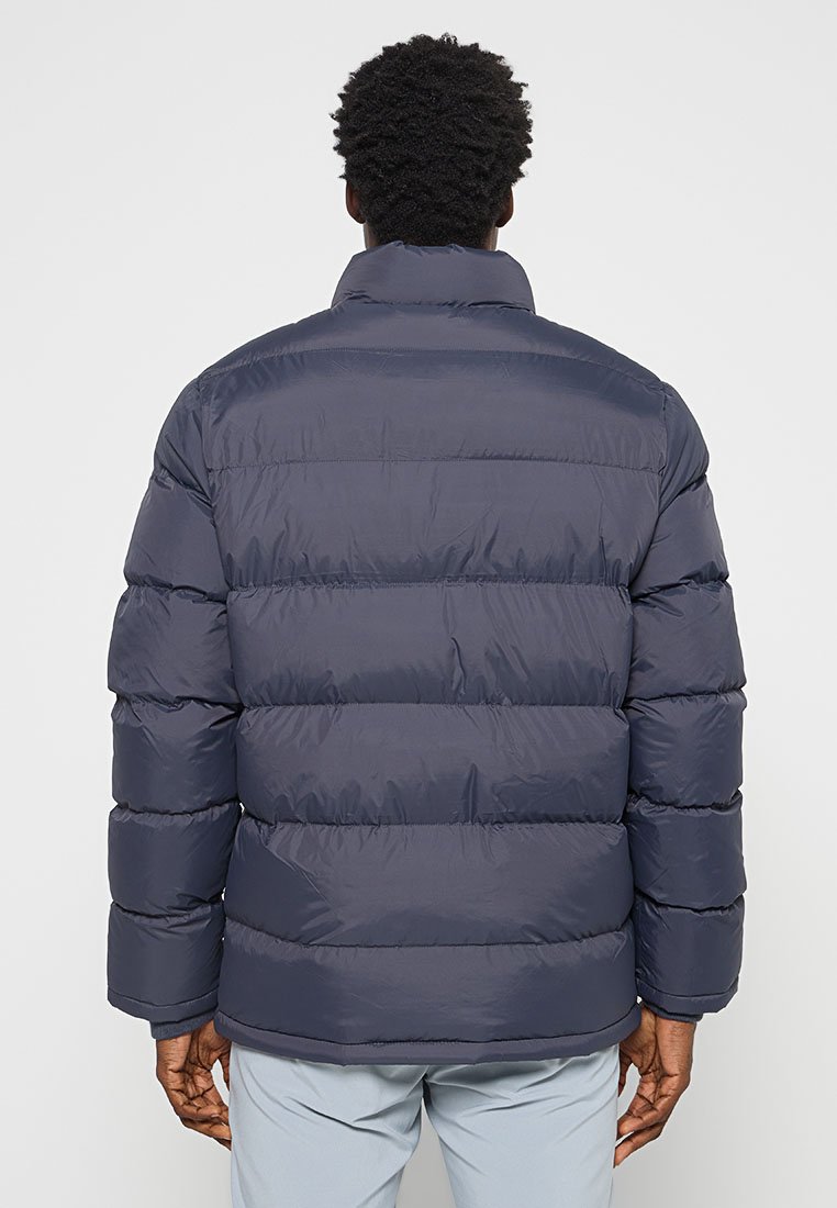 Veste rembourrée marine foncé avec un col haut, présentant des sections matelassées horizontales, des poignets côtelés et une finition lisse et brillante.