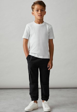 Camiseta blanca de manga corta combinada con pantalones cargo negros que tienen bolsillos laterales y puños elásticos, completado con zapatillas blancas.