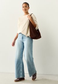 Vaaleanbeige pitkähihaista yläosaa, vaaleansiniset korkeavyötäröiset leveälahkeiset farkut, ruskea mokkanahkainen olkalaukku ja tummanruskeat lenkkarit valkoisilla yksityiskohdilla.