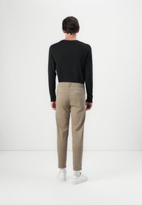 Schwarzes Langarmshirt mit Rundhalsausschnitt, kombiniert mit beigen Hosen mit elastischem Bund und zwei Gesäßtaschen. Weiße Sneaker.