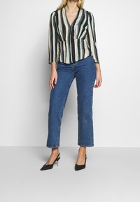 Pasek bluzka w czarno, zielono i kremowo, dekolt w kształcie litery V, rękawy trzyczwarte, zestawiona z niebieskimi dżinsami o prostym kroju i czarnymi szpilkami.