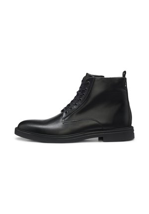 Schwarzer Leder-Stiefel mit Schnürung vorne und flacher Sohle, seitlich auf weißem Hintergrund dargestellt.