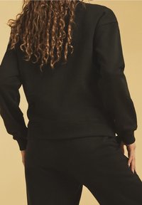 Zwarte sweatshirt met een relaxte pasvorm, geribde manchetten en onderrand, gemaakt van zachte stof. Heeft een ronde halsontwerp en een minimalistische stijl.