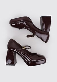 Tacones de plataforma de charol burdeos con amplios tacones de bloque, puntera redonda y tira en el tobillo con un pequeño detalle de hebilla dorada.