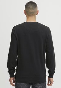 Black crewneck sweatshirt with long sleeves, ribbed cuffs, and hem. Made from soft fabric with a smooth texture. Minimal design.