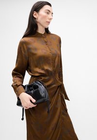 Abito marrone con motivo, dalla vestibilità tailored, maniche lunghe e colletto a revers. Abbinato a una piccola borsa nera con cordoncino.