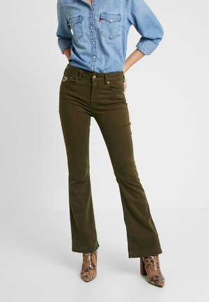 Personne portant un pantalon évasé taille haute vert olive, une chemise en denim clair à boutons avec les manches retroussées, et des bottes à talons marron imprimé serpent.