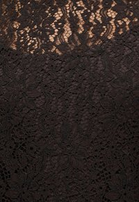 Tissu en dentelle florale noire sur une peau claire, montrant des motifs complexes et une texture avec une apparence transparente et délicate.