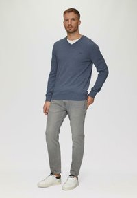 Blauer V-Ausschnitt-Pullover aus weichem Strickstoff; kombiniert mit hellgrauen Jeans und weißen Sneakers; lässige Passform mit gerippten Bündchen und Saum.