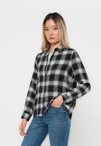 Svart og hvit rutete skjorte i løs passform med knapper og spiss krage. Kombinert med blå jeans, fremstår stoffet mykt og med tekstur.