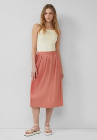 Plissé midi-rok in koraal, met een gladde tailleband en verticale plooien. Gecombineerd met een lichtgele tanktop en witte sandalen.