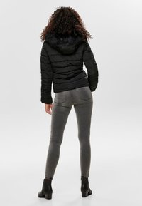 Svart pufferjacka med huva som har fake pälskant, tillsammans med grå smala jeans och ankelstövlar. Jackan har en kviltad textur.