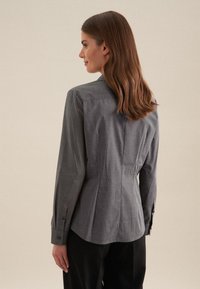 Grau longsleeve Hemd mit tailliertem Schnitt, ausgestattet mit einem spitzen Kragen und subtiler Textur. Enthält Knopfakzente an den Bündchen und Rückenfalten.