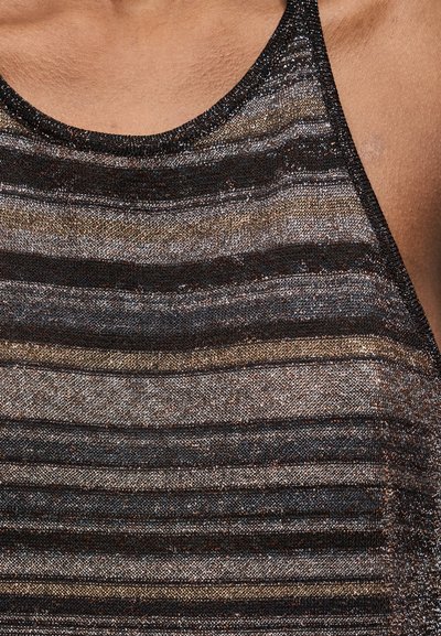 Κοντινό πλάνο του επάνω μέρους του στήθους ενός ατόμου που φορά αμάνικο, λαμπερό τοπ με οριζόντιες μεταλλικές μαύρες, χρυσές και ασημί ρίγες.