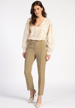 Beige textuur blouse met een ronde hals, gecombineerd met op maat gemaakte kaki broeken met een voorknop en splitrokken, gedragen met lichtbeige hakken.
