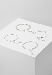 Keturi sidabriniai apyrankės, turinčios įvairius dizainus: grandinės stiliaus, barų grandinė, karoliukų akcentas ir plokščių grandinių raštas, visi su etiketėmis.