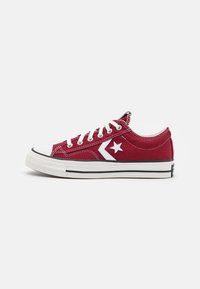 Rote Canvas-Sneaker im Low-Top-Stil mit weißen Schnürsenkeln, Gummikappe, schwarz-weißer gestreiften Sohle und einem weißen Stern-Logo an der Seite.
