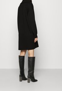 Svart oversize klänning med bred krage, långa ärmar och en böjd fåll. Matchas med knähöga svarta läderstövlar med texturerade klackar.