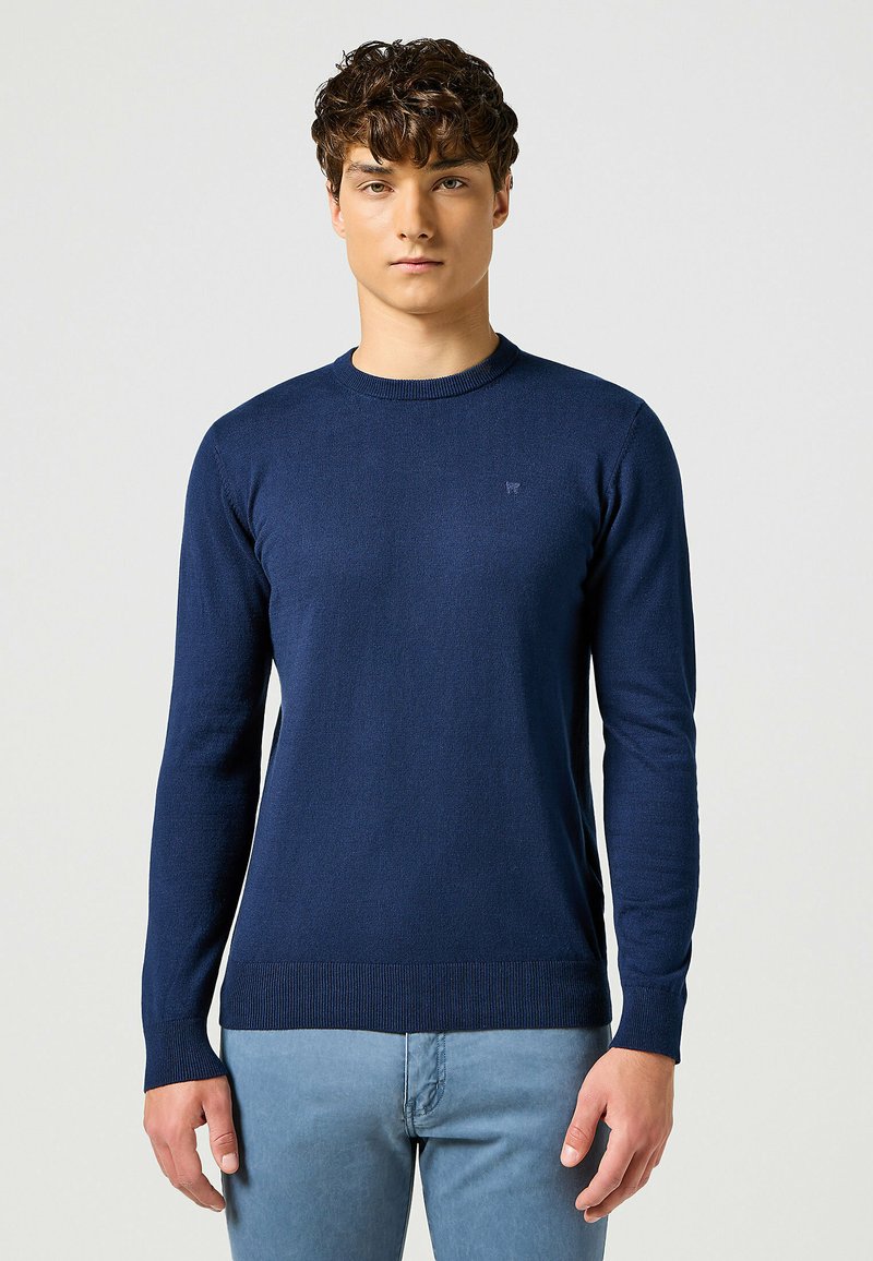 Maglione a maglia blu navy con scollo a girocollo, maniche lunghe e orlo a coste. Presenta un logo sottile sul petto. Texture morbida.