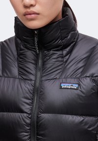 Gros plan d'une personne portant une doudoune noire Patagonia avec un col montant et une fermeture éclair visible.