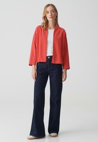 Veste légère corail à l'avant ouvert, coupe décontractée, manches trois-quarts ; associée à un pantalon flare en denim foncé taille haute.