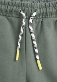 Gröna sweatpants med en mjuk textur, elastisk midja och dragsko med ett svartvitt rutmönster och gula spetsar.