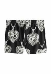Shorts noirs avec des médaillons en forme de cœur blanc répétitifs, ornés de motifs floraux et de chaînes imprimés sur le tissu.