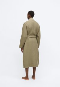 Accappatoio verde oliva con trama a cialda, cintura in vita e maniche lunghe, dotato di colletto e taglio al ginocchio.