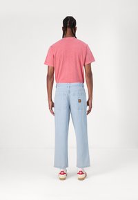 Φωτεινά μπλε τζιν παντελόνια με φαρδιές γραμμές, δύο πίσω τσέπες και λογότυπο. Συνδυασμένα με κοντομάνικο ροζ μπλουζάκι και αθλητικά παπούτσια.