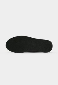 Semelle de chaussure noire avec surface texturée antidérapante vue du dessous sur fond blanc.