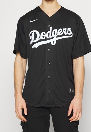 Mężczyzna ubrany w czarną koszulę baseballową Dodgers na guziki z białym napisem i małym białym logo Nike na piersi.