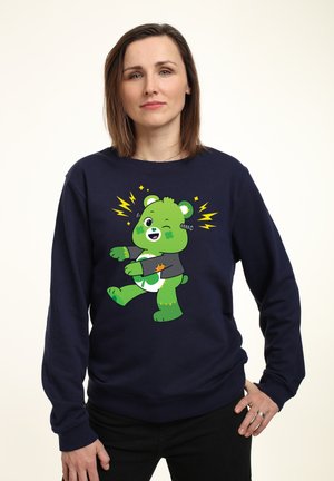 Mørkeblå sweatshirt med en grøn tegneseriebjørn, der har en grå dragt, fremhævet af lynbolte og legesyge ansigtsudtryk.