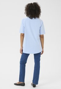 T-shirt oversize azzurro chiaro con maniche raglan corte, abbinato a jeans dritti blu scuro e ballerine nere. Design minimalista, texture morbida.