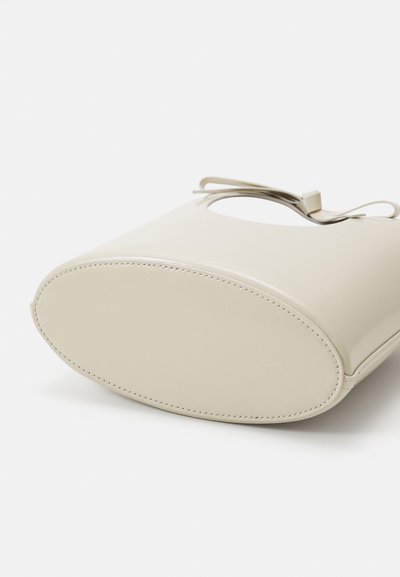 Beige handbag with a smooth, glossy texture, rounded shape, and an open handle. Features visible stitching along the edges.